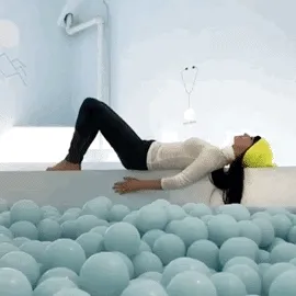 Animated gif of a woman in white reclining back into a pool of pale blue balls