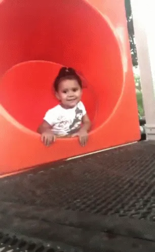 Animated gif of a smiling toddler sliding out of a red playground tube slide
