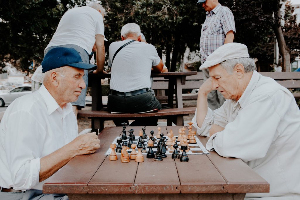 two senior men playing chess at a bench